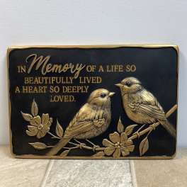 Memorial plaque with two birds and gold lettering on a black background