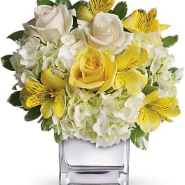 Yellow and white flower arrangement in a clear square vase