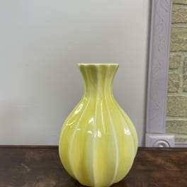 Yellow ceramic vase with a fluted neck on a wooden surface