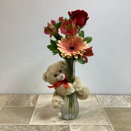 Teddy bear beside a vase of red and peach flowers