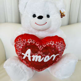 White teddy bear holding a red heart pillow with the word Amor