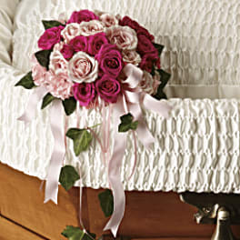 Pink and white rose bouquet with ribbon draped over a white casket