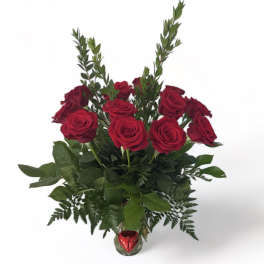 Red roses arranged in a clear glass vase with a red heart ornament