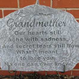 Gray memorial stone engraved for grandmother against a brick wall