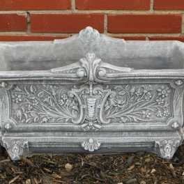 Ornate gray stone planter box against a brick wall