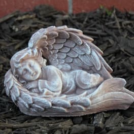 Small sleeping angel figurine with wings, resting on dark mulch