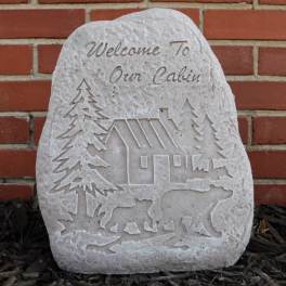 Carved stone plaque with a cabin, trees, and bears against a brick wall