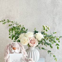 White and blush roses in a ribbed vase with a plush bunny and card