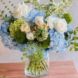 Blue hydrangeas and white roses arranged in a clear glass vase