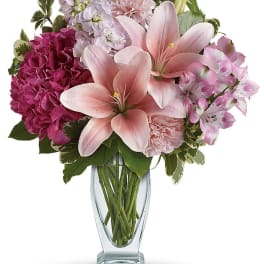 Pink lilies and mixed blooms arranged in a clear glass vase