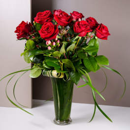 Red roses arranged in a tall glass vase with greenery