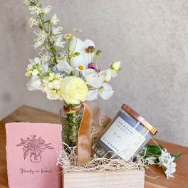 Small flower arrangement in a glass jar with a candle and pink card in a gift box