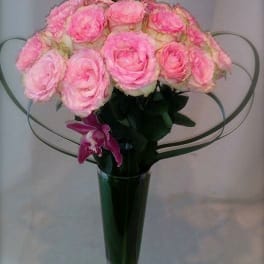 Pink roses arranged in a tall glass vase with wire heart loops