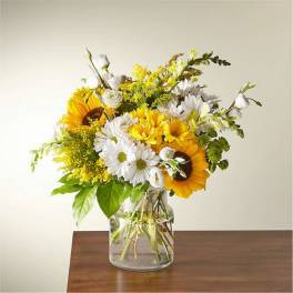 Yellow and white sunflower and daisy arrangement in a clear glass vase on a wooden table