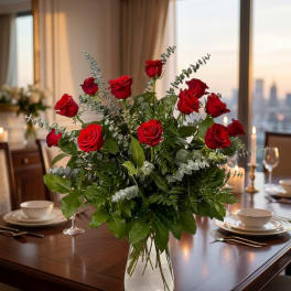 Red roses arranged in a clear glass vase with mixed greenery