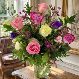 Mixed roses in pink, purple, and yellow arranged in a glass vase