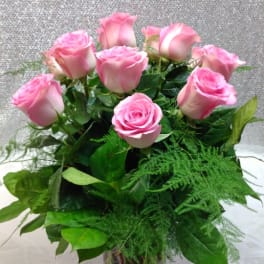 Pink roses arranged in a clear glass vase with greenery