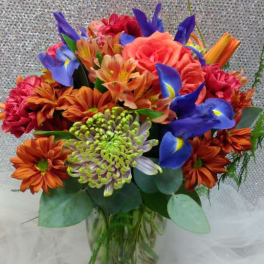 Mixed bouquet of orange, pink, and blue flowers in a glass vase