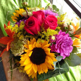 Bouquet of red roses, sunflowers, and purple blooms in a vase