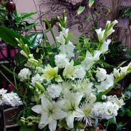 Tall all-white floral arrangement with lilies, carnations, and other blooms in a ceramic container