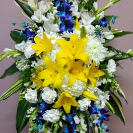 Tall floral standing spray with yellow lilies, white blooms, and blue orchids