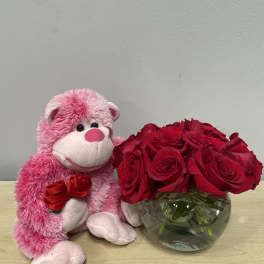 Pink teddy bear beside red roses in a glass bowl vase