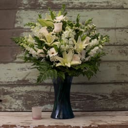 White floral arrangement in a dark blue vase with a small candle beside it