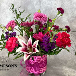 Mixed pink and purple bouquet in a clear glass vase with a ribbon