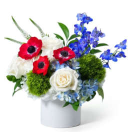 Low red, white, and blue flower arrangement with roses and anemones in a white cylinder vase