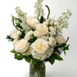 Tall arrangement of white and cream roses, hydrangeas, and delphinium in a clear glass vase