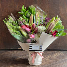 Mixed bouquet of lilies, pink blooms, and white flowers wrapped in paper