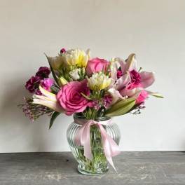 Pink and white mixed bouquet in a clear glass vase with a pink ribbon