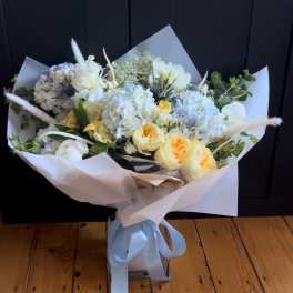 Bouquet of white and pale yellow flowers wrapped in white paper with a blue ribbon