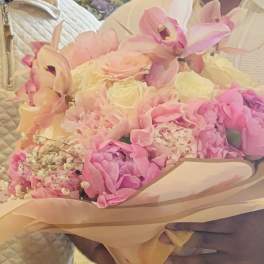 Pink and cream bouquet with orchids, roses, and hydrangeas wrapped in beige paper