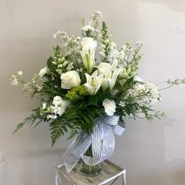 White lilies and roses in a glass vase with a striped ribbon