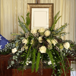 Large white rose arrangement with mixed greenery in front of a framed display