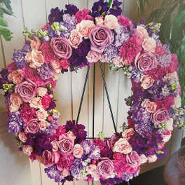 Heart-shaped floral wreath in pink, lavender, and purple blooms on a black stand