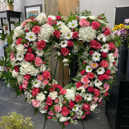 Large heart-shaped floral wreath with pink and white flowers on a stand