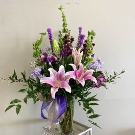 Tall bouquet of pink lilies and purple flowers in a glass vase
