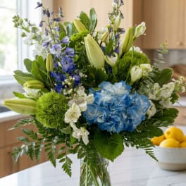 Blue hydrangeas and white lilies in a clear glass vase