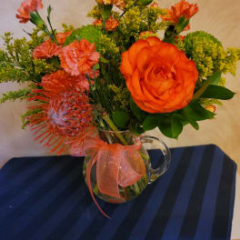 Orange and pink mixed bouquet in a glass pitcher vase with ribbon