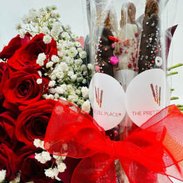 Red roses with white baby's breath beside chocolate-covered pretzels in a clear wrap