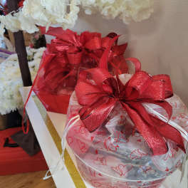 Gift baskets wrapped in heart-patterned cellophane with red bows and white flowers above