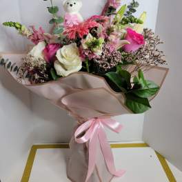 Pink and white bouquet with roses, lilies, and a teddy bear topper