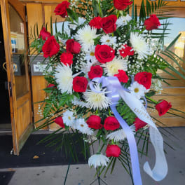 Standing floral spray with red roses and white daisies on a ribboned easel