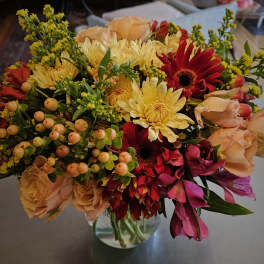 Mixed bouquet of yellow, red, and peach flowers in a glass vase
