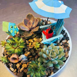 Succulent arrangement in a white bowl with a tiny beach chair and umbrella