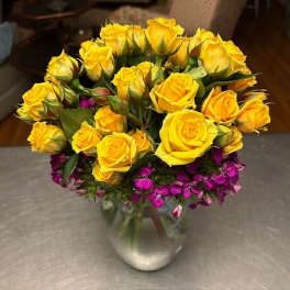 Yellow roses and small purple flowers arranged in a clear glass vase