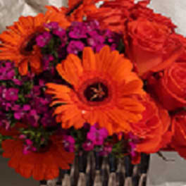 Orange gerbera daisies and red roses with purple filler flowers in a basket