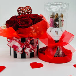 Red roses in a striped box beside chocolate-covered pretzel sticks